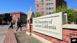 Orang-orang berjalan melintasi papan tanda di wilayah University Village di University of Southern California di Los Angeles pada 12 Maret 2019. (Foto: AP)
