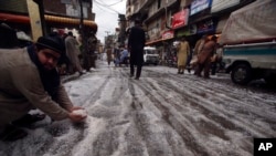 Seorang pria meraup butiran-butiran es setelah hujan es di Peshawar, Pakistan, Sabtu, 30 Maret 2024. (Foto: Mohammad Sajjad/AP Photo)