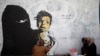 FILE - A friend of artist Haifa Subay takes pictures of her painting a mural she says represents the children and women suffering in Yemen's war, in Sanaa, Yemen, Feb. 21, 2019.